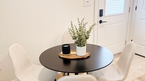 Una mesa redonda para comer con cuatro sillas blancas, una planta en maceta y una vela sobre una bandeja de madera.