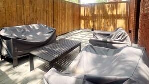 Un porche cubierto con un pérgola de madera, una parrilla y mobiliario de exterior.