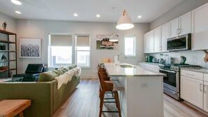 A modern kitchen with white cabinets, a central island, and a built-in microwave. - East Nash Lux - 13 Beds City Views (Nashville)