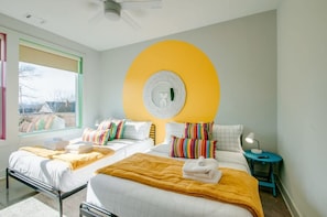 A hotel room with two beds, a large window, a circular wall decoration, and a bedside table with a lamp.