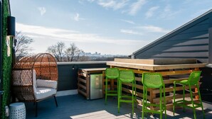 A deck with a wooden table and chairs, a wicker chair, and a trash can. - East Nash Lux - 13 Beds City Views (Nashville)