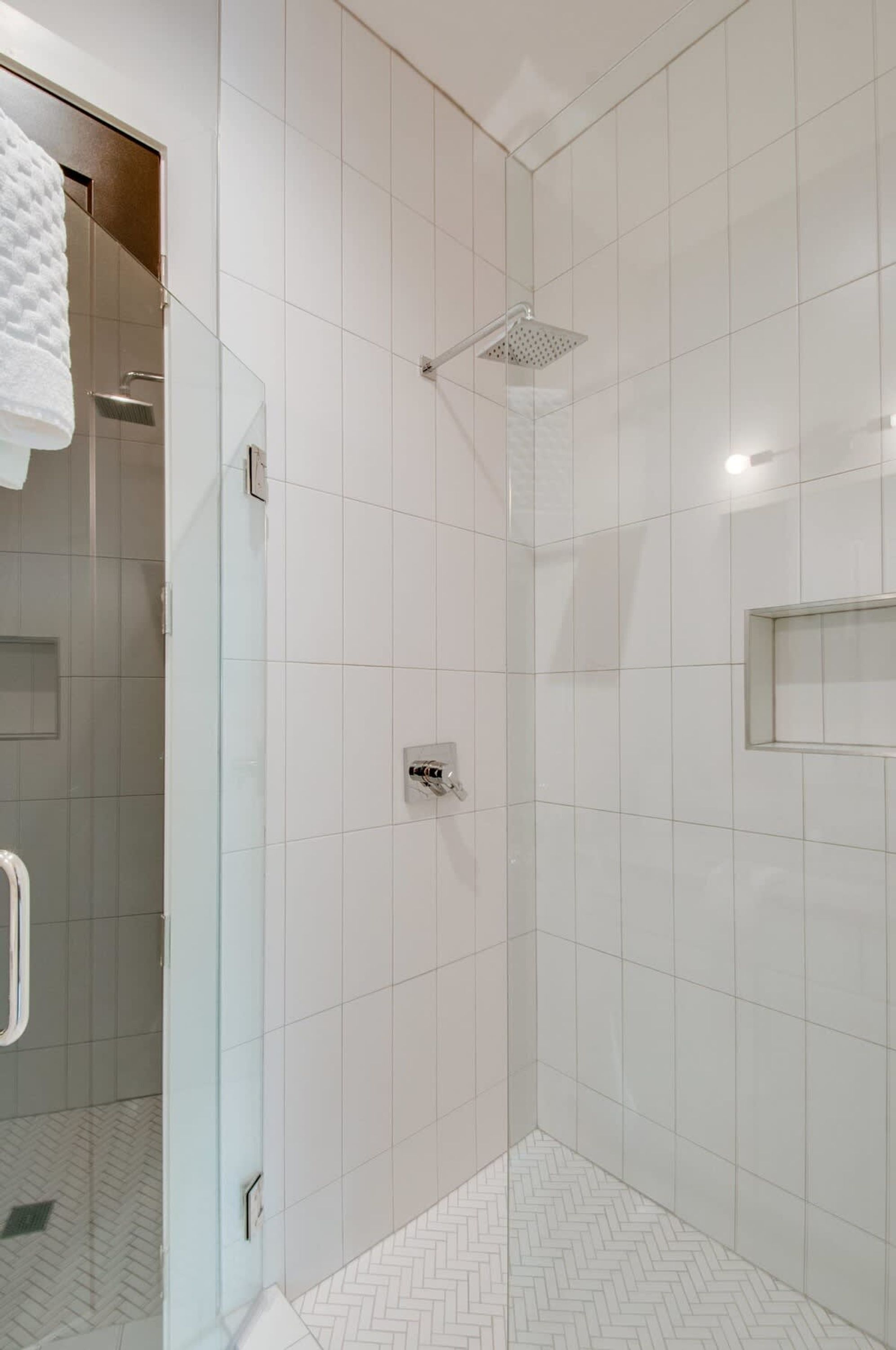 A modern shower with a square showerhead, a glass door, and a herringbone-patterned floor.