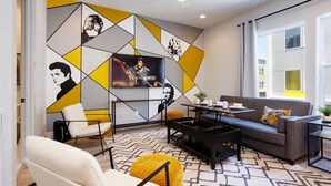 A modern living room with a geometric wall design, a sofa, a coffee table, and a TV. - East Nash Oasis - 13 Beds - Going Fast (Nashville)