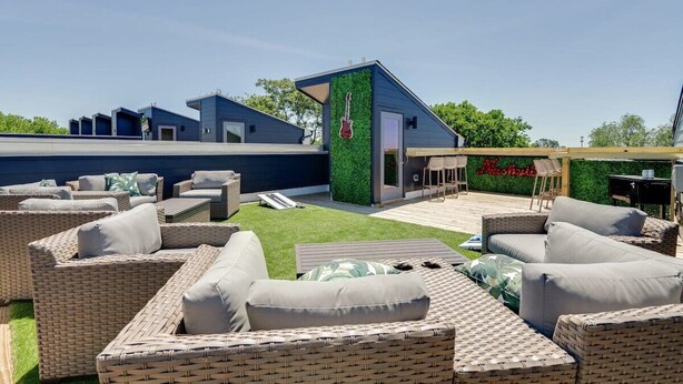A modern outdoor seating area with wicker furniture and a green wall with a guitar decoration. - East Nash Oasis - 13 Beds - Going Fast (Nashville)