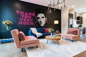 Un salon moderne avec un néon, des canapés, une table basse et une cuisine en arrière-plan.