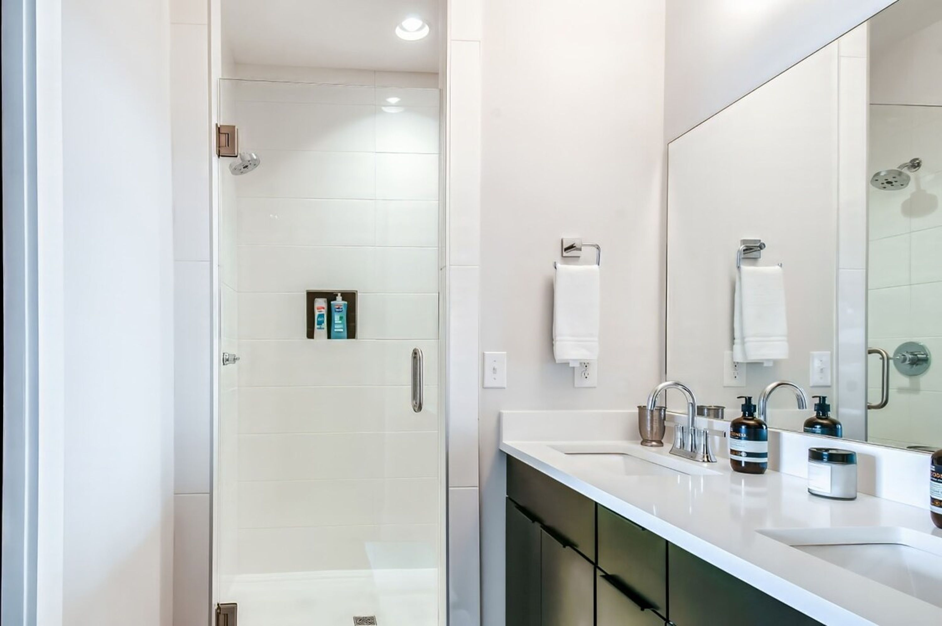 A modern bathroom with a glass-enclosed shower, a large mirror, and a vanity with a sink and toiletries.