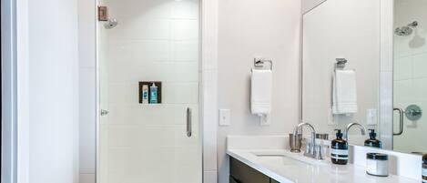 A modern bathroom with a glass-enclosed shower, a large mirror, and a vanity with a sink and toiletries.