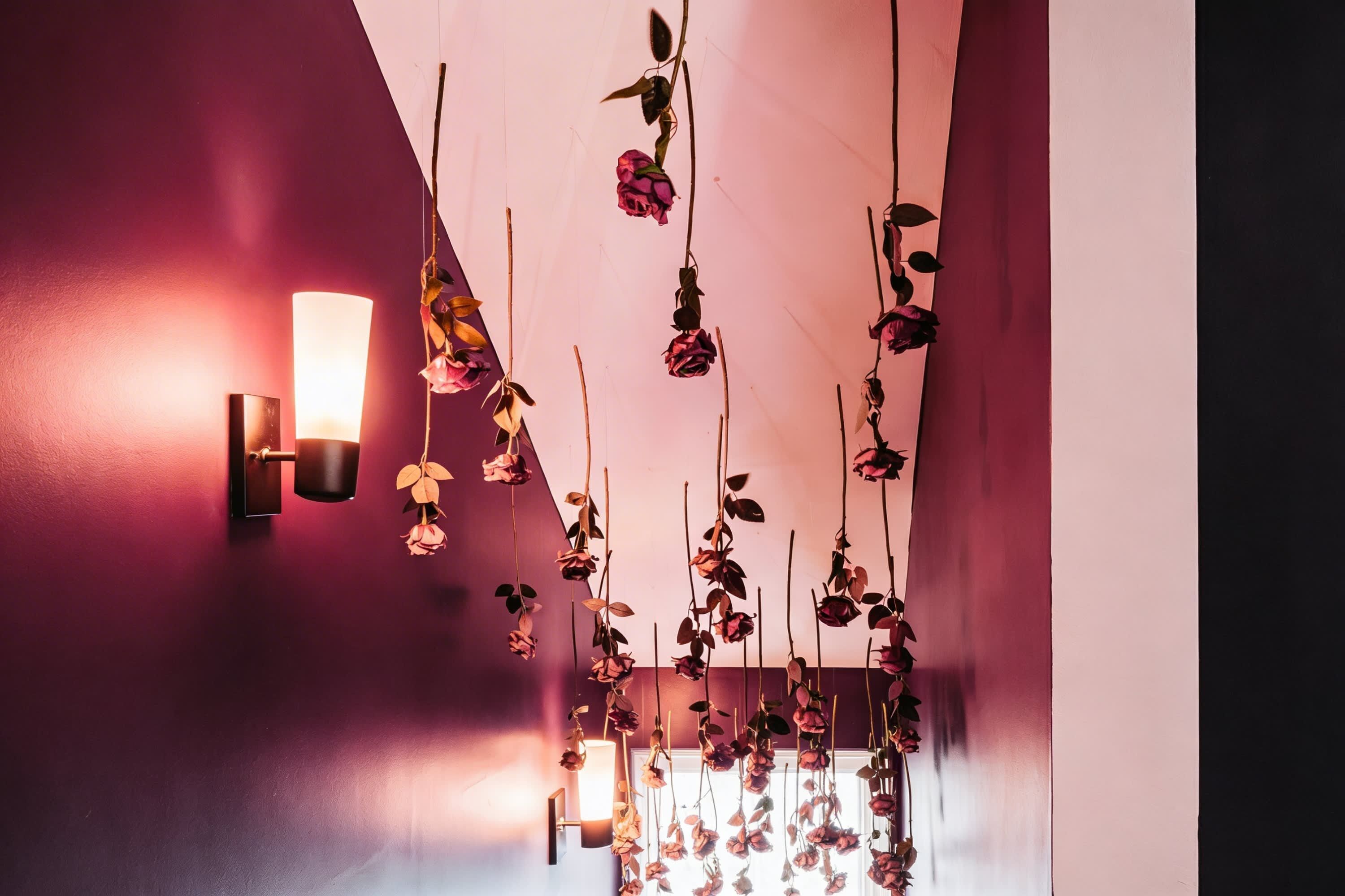 Corredor com luminária na parede e decorações florais penduradas.