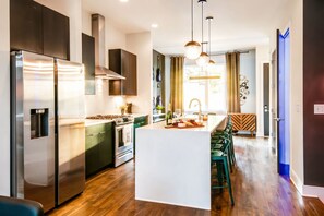 Una cocina moderna con electrodomésticos de acero inoxidable, una isla central con taburetes de bar y una zona de comedor con mesa de diseño en patrón de espiga.