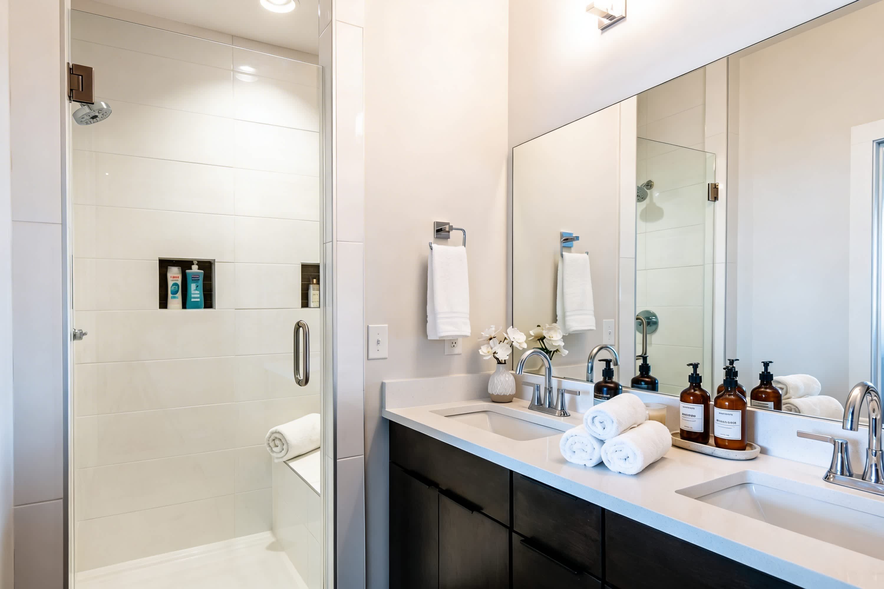 A modern bathroom with a walk-in shower, a large mirror, and a vanity with a sink and toiletries.