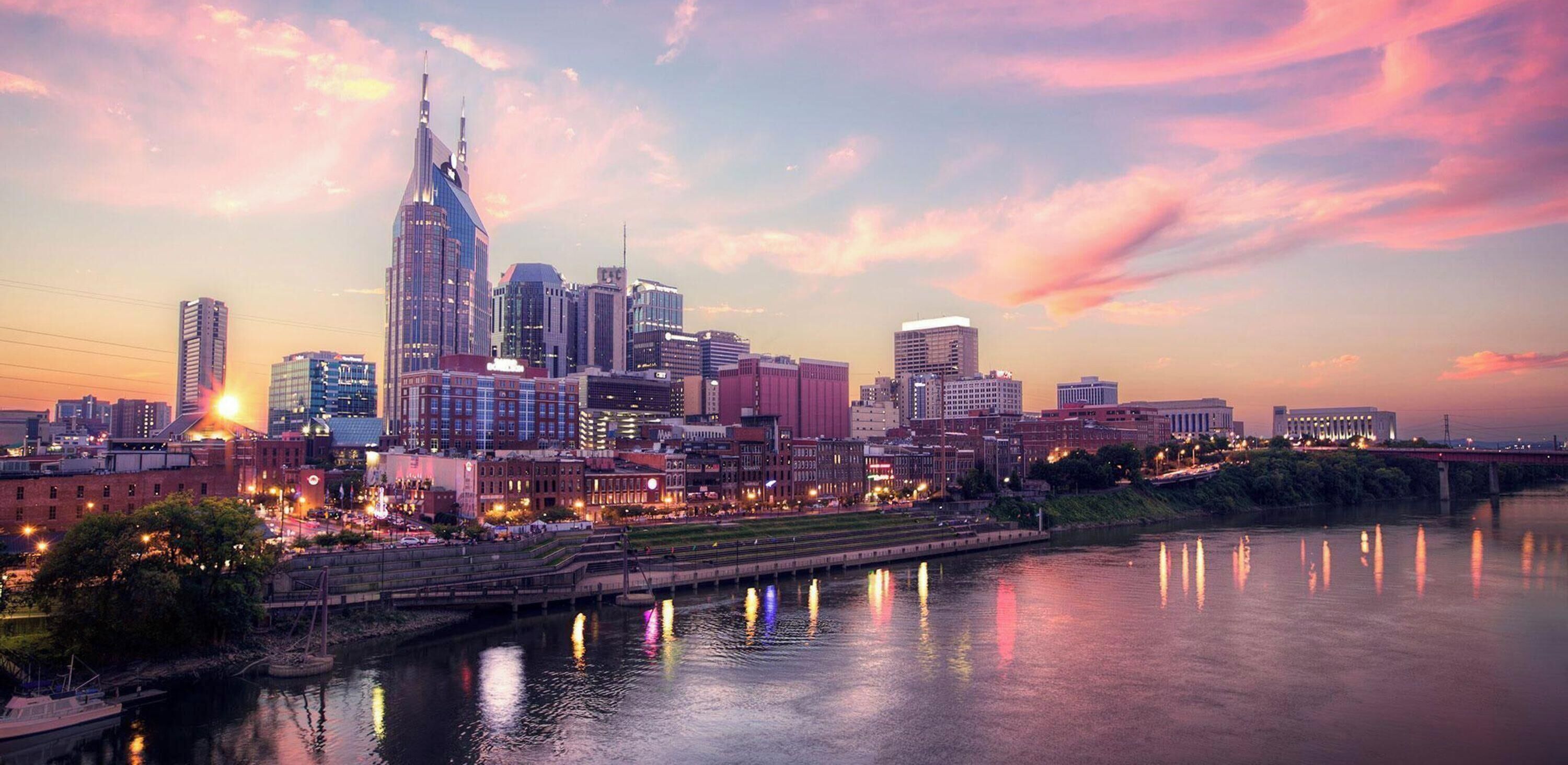 A city skyline at dusk with a river in the foreground.