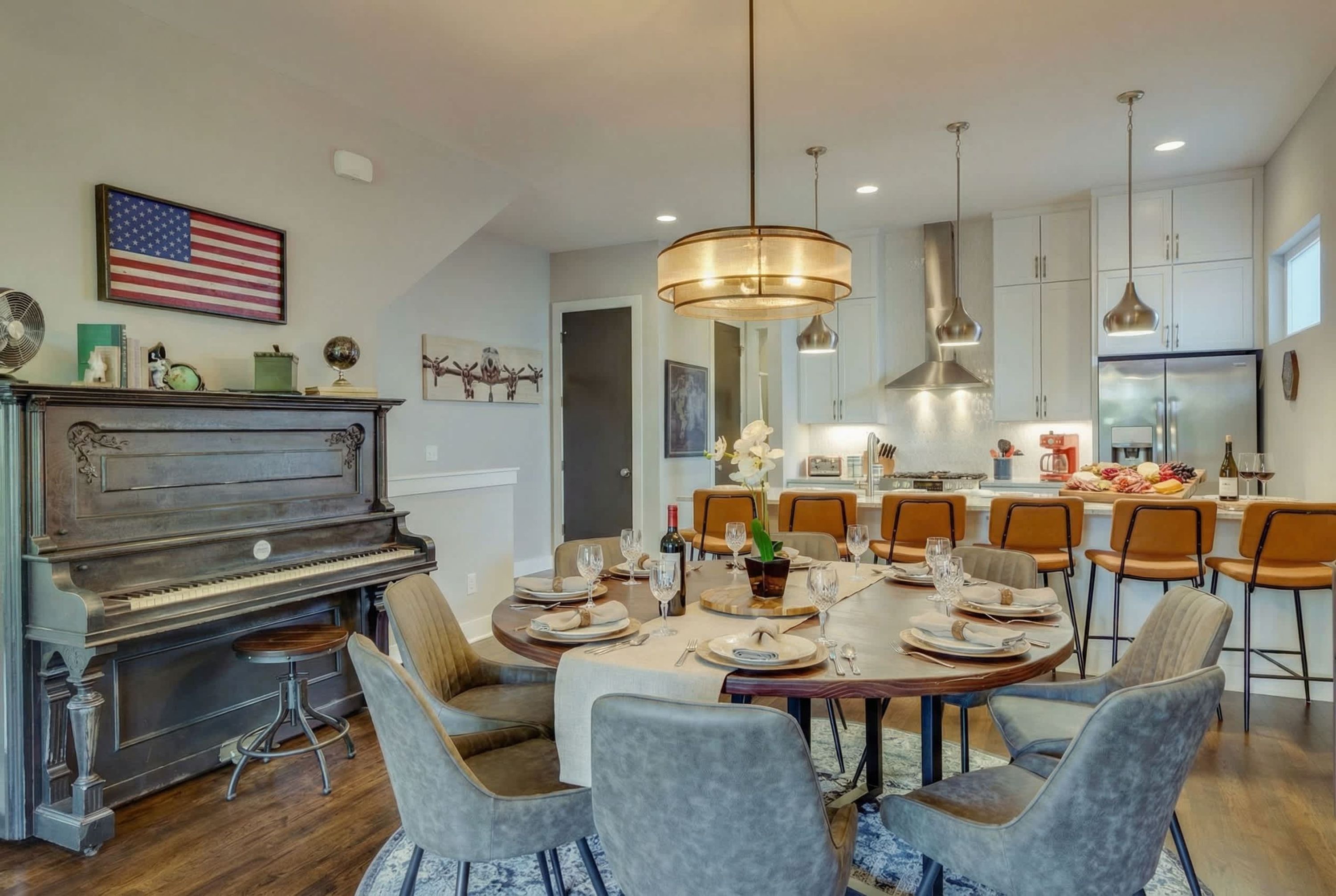 A dining area with a piano, a large chandelier, and a kitchen in the background.
