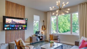 A modern living room with a flat-screen TV, a guitar, and a sofa with cushions.