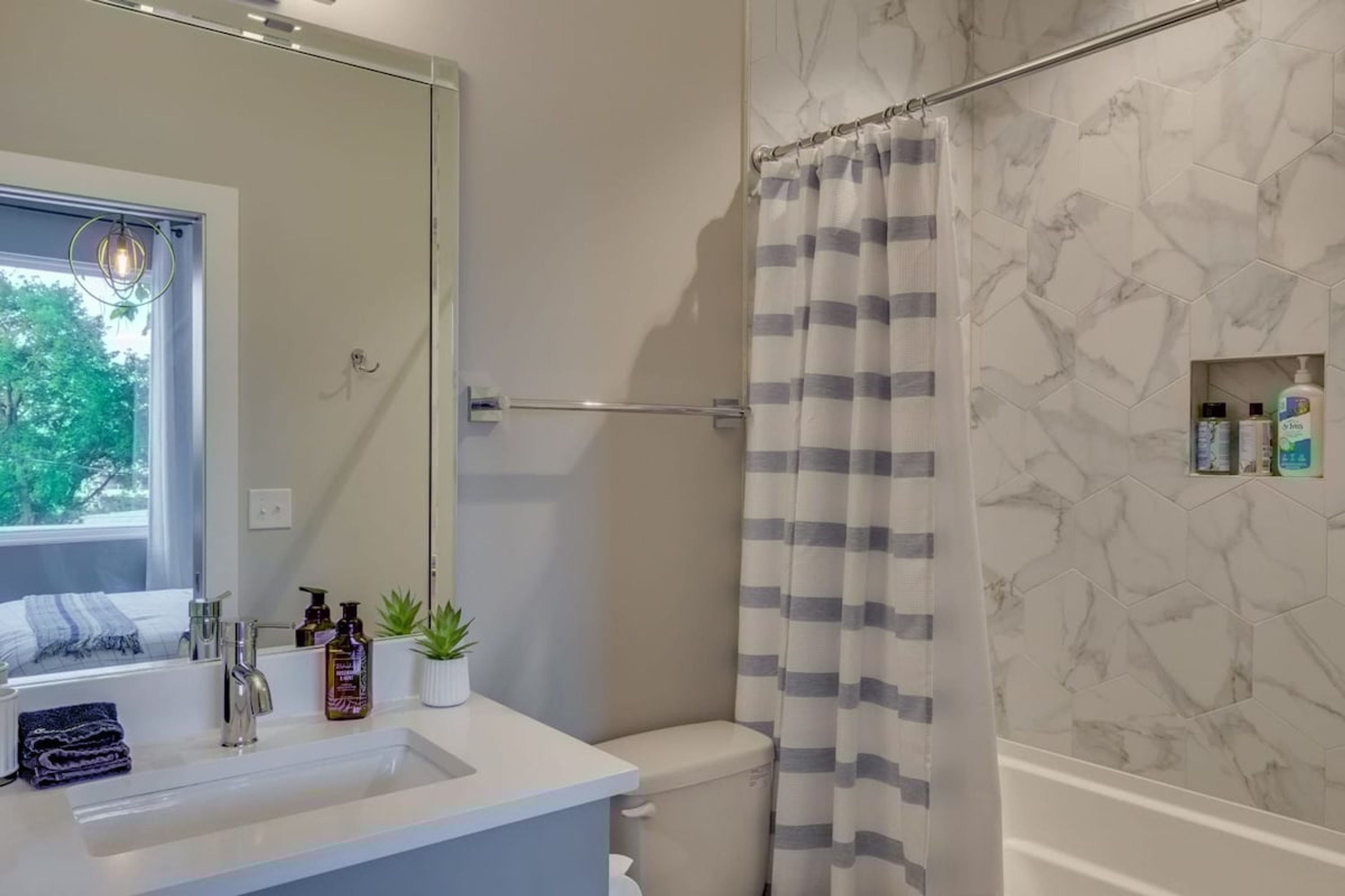 Un baño con un lavamanos blanco, un espejo, una cortina de ducha y artículos de aseo en la pared.