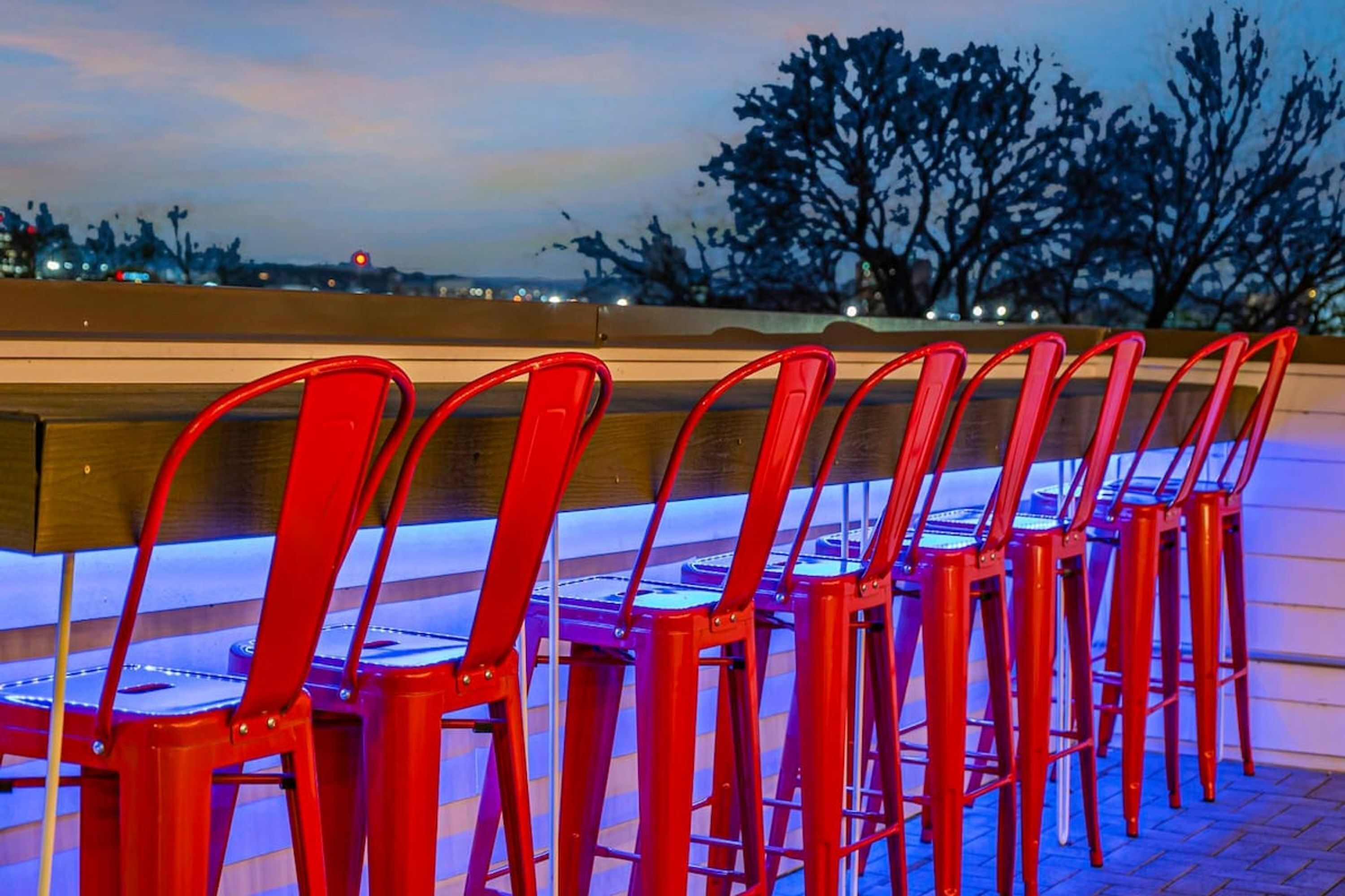 A row of red chairs with a view of a cityscape at dusk.