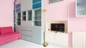 A living room with a pink sofa, a TV, a floor lamp, and a white cabinet. - GuestHost - Island Cosy Pink Studio Apt (Milano)