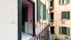 A balcony with a metal railing, a pink door, and a beige building facade. - GuestHost - Island Cosy Pink Studio Apt (Milano)