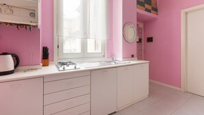 A pink-themed kitchen with a gas stove, sink, and white cabinets. - GuestHost - Island Cosy Pink Studio Apt (Milano)