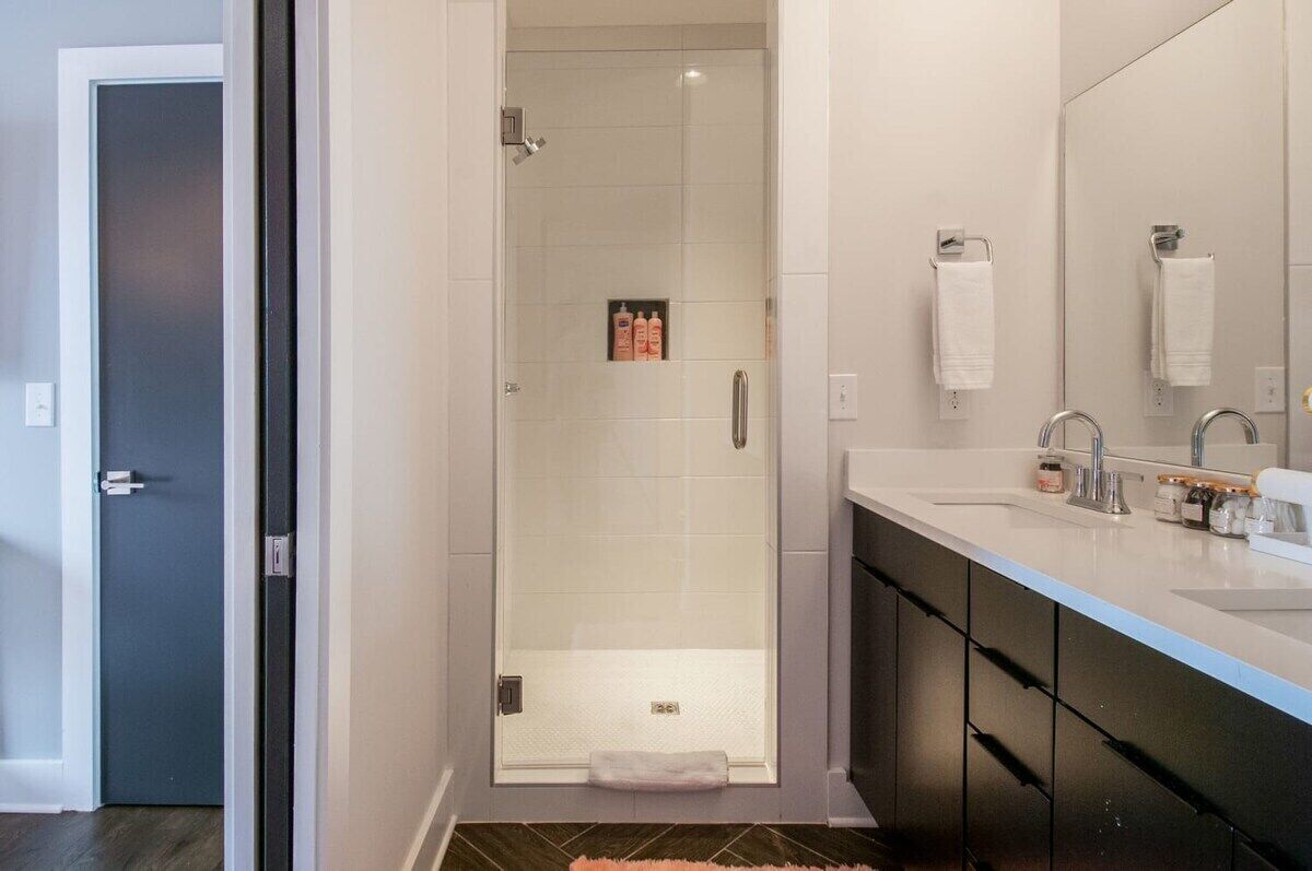 Une salle de bain moderne avec une douche à parois de verre, un grand miroir et un meuble-lavabo doté d’un évier et d’un porte-serviettes.