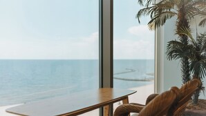 A wooden table and chair by a large window overlooking the ocean.