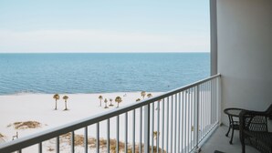A balcony with a view of the ocean and a sandy beach with palm trees.