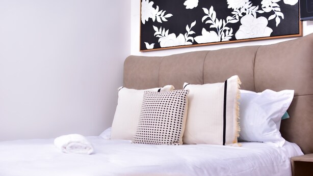 A neatly made bed with white linens, a beige headboard, and a floral-patterned wall art above. - Luxe Nairobi Escape, Walk to Swahili Eats & Mall & 15 minutes drive to Park. (Nairobi)