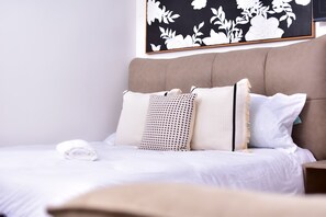 A neatly made bed with white linens, a beige headboard, and a floral-patterned wall art above. - Luxe Nairobi Escape, Walk to Swahili Eats & Mall & 15 minutes drive to Park. (Nairobi)
