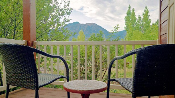 A balcony with two wicker chairs and a small table, overlooking a mountain and greenery.