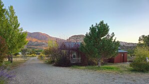 A gravel driveway leading to a rustic cabin with a porch, surrounded by trees and mountains in the background.
