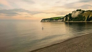 Een rustig strand met een persoon op een paddleboard, kliffen op de achtergrond en een heldere lucht.