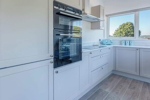 A modern kitchen with white cabinetry, a built-in oven, and a window with a view of the outdoors. - River View Prime River Front Location (Seaton)