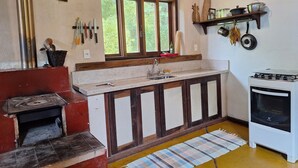 Cocina rústica con estufa de leña, un lavabo y una ventana con vistas a la vegetación.