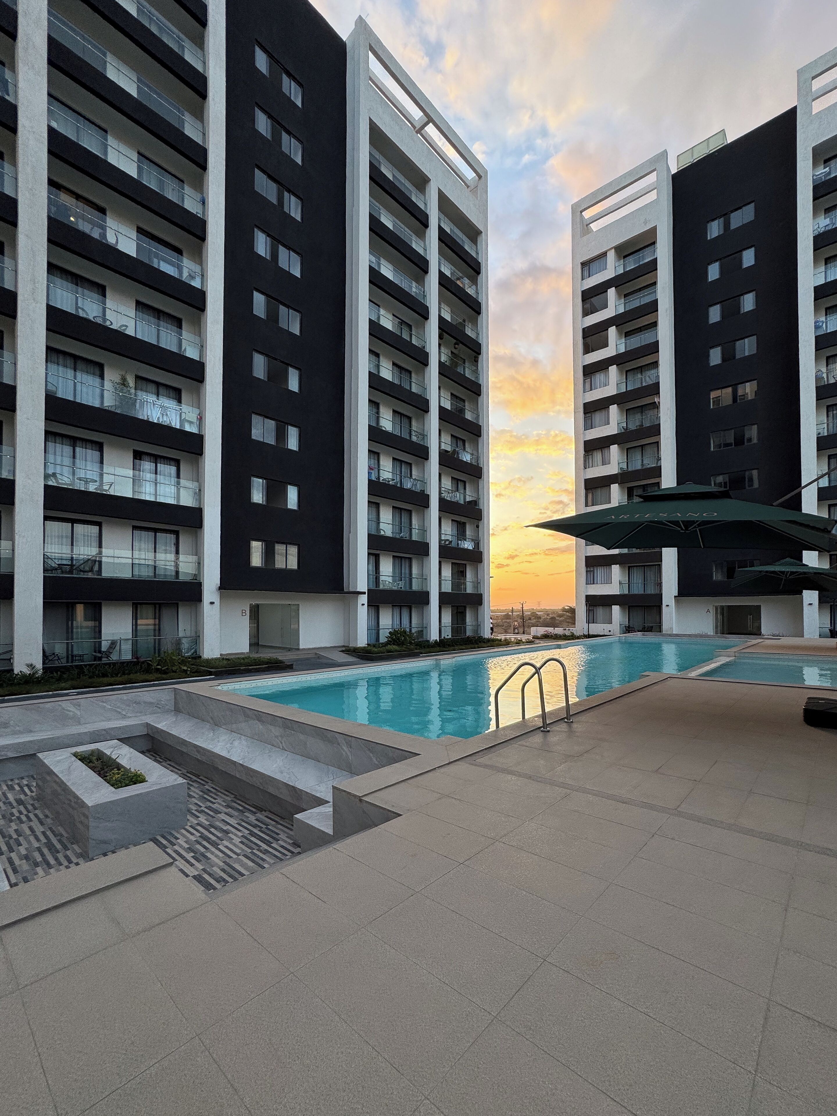 A modern apartment building with a swimming pool, balconies, and a sunset view.