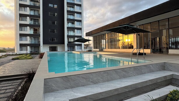 A modern hotel with a swimming pool, a covered area, and a large building in the background. - Studio apartment in Nairobi, close to JKIA airport and SGR, WiFi, pool & gym (Nairobi)