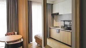 Une cuisine moderne avec des meubles en bois et une hotte noire, un coin repas avec une table ronde et des chaises, et une grande fenêtre avec des rideaux.