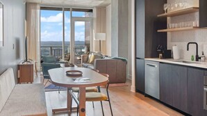Une cuisine moderne dotée d’un four encastré, un coin repas avec une table ronde et des chaises, un canapé et une vue sur la ville grâce à de grandes fenêtres.