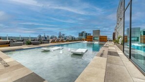 Une piscine à débordement située sur le toit, dotée de chaises longues, offrant une vue sur les toits de la ville et présentant une architecture moderne.