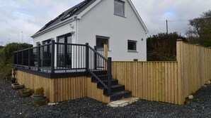 Une maison moderne à deux étages, dotée d’une terrasse en bois et de rampes noires.