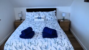 Un lit recouvert d’une couvre-lit à motifs floraux, avec deux oreillers et une plaque portant l’inscription « CORNWALL » fixée au chevet.