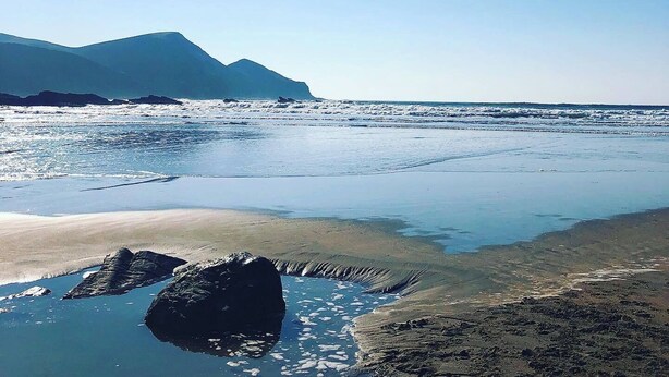Une plage avec un ciel dégagé, une eau calme et des montagnes à l’horizon.