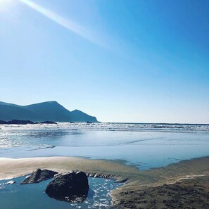 A beach with clear skies, calm water, and distant mountains.