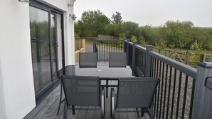Un balcon avec une table et des chaises, une clôture en bois et une vue sur la verdure.