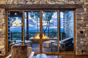 Habitación con paredes de piedra y un amplio ventanal que da a una terraza exterior con una chimenea y asientos.