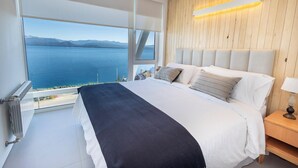 A bedroom with a large bed, a wooden headboard, a nightstand, and a view of the sea. - B612 Bariloche (San Carlos de Bariloche)