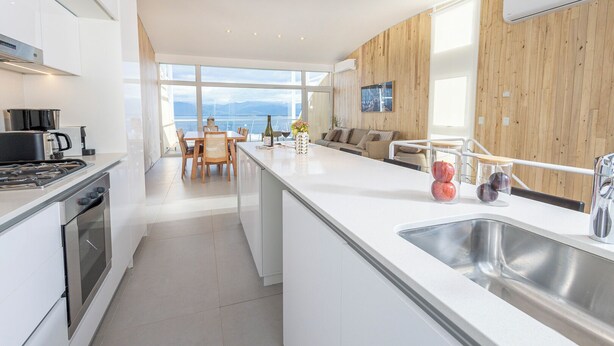 A modern kitchen with white cabinetry, a large island with a sink, and a dining area with a view. - B612 Bariloche (San Carlos de Bariloche)