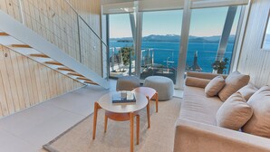 A modern living room with a sofa, ottoman, and table, a staircase, and a large window with a view of the sea and mountains. - B612 Bariloche (San Carlos de Bariloche)