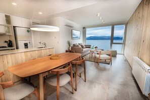 Uma cozinha moderna com uma mesa e cadeiras de madeira, um espaço de refeições com vista para o mar e uma área de estar aconchegante com um sofá e uma mesinha de centro.