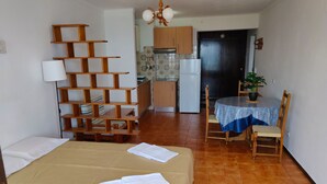 A room with a bed, a wooden shelf unit, a dining table with chairs, a kitchen area, and a potted plant. - Studio apartment with stunning sea views in the heart of the city (Albufeira)