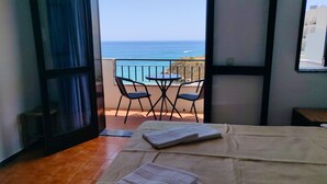 A bedroom with a bed, a small table, two chairs, and a view of the ocean through an open door. - Studio apartment with stunning sea views in the heart of the city (Albufeira)