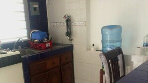 A kitchen with a stove, cabinets, a water dispenser, and a chair.